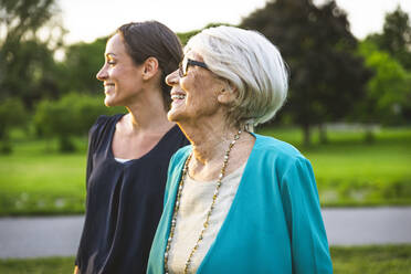 Lächelnde Großmutter schaut weg, während sie bei ihrer Enkelin im Park steht - OIPF00987
