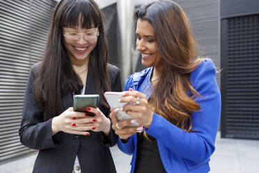 Businesswomen smiling while using mobile phones - IFRF00859