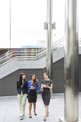 Female colleagues discussing while walking on footpath - IFRF00862