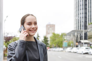 Geschäftsfrau lächelnd im Gespräch am Handy in der Stadt - IFRF00869