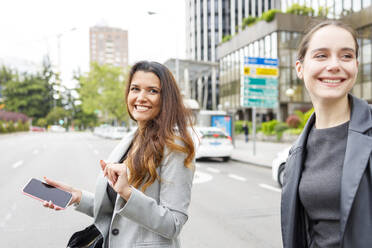 Businesswoman with mobile phone walking on road with colleague in city - IFRF00873