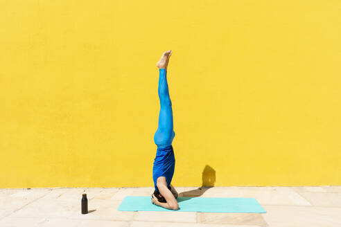 Mann übt Salamba Shirshasana, während er an einer gelben Wand Yoga macht - RFTF00086