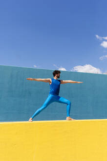 Mann übt Virabhadrasana II, während er Yoga an einer Stützmauer macht - RFTF00093