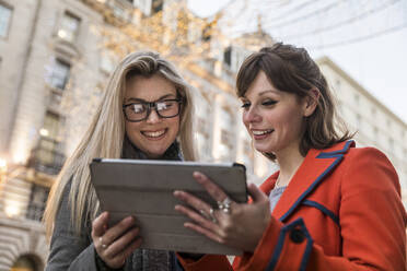 Smiling young women sharing digital tablet while standing in city - WPEF04828