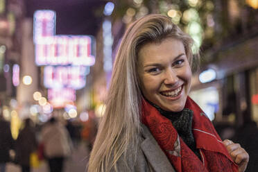 Cheerful blond woman wearing red scarf while standing in city - WPEF04838