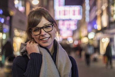 Fröhliche junge Frau mit braunem Haar, die eine Brille trägt und in der Stadt steht - WPEF04839