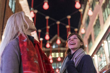 Lächelnde Freundinnen mit Blick auf die Weihnachtsbeleuchtung während der Feiertage - WPEF04840