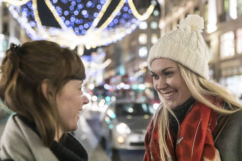 Lächelnde blonde Frau mit Strickmütze, die ihre Freundin anschaut, während sie sich über Weihnachten unterhält - WPEF04843