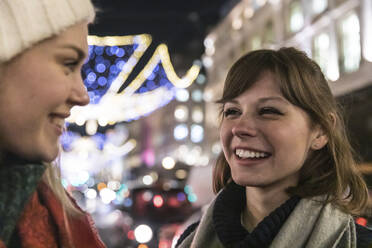 Lächelnde junge Frau mit braunem Haar, die ihre Freundin anschaut, während sie über Weihnachten spricht - WPEF04844
