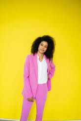 Afro businesswoman with hand on hip standing in front of yellow wall - KNSF08693