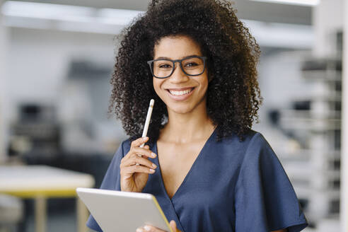 Lächelnde Unternehmerin mit digitalem Tablet und digitalisiertem Stift im Büro stehend - KNSF08727
