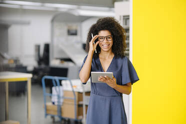 Lächelnde Geschäftsfrau mit digitalem Tablet, die eine Brille im Büro einstellt - KNSF08730