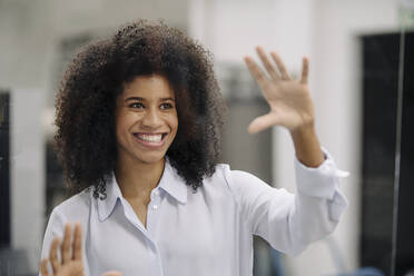 Smiling Afro businesswoman seen through glass in office - KNSF08736