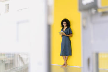 Lächelnde Unternehmerin hält digitales Tablet vor einer Wand im Büro - KNSF08738