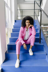 Female entrepreneur with hand on chin sitting on steps at office - KNSF08752