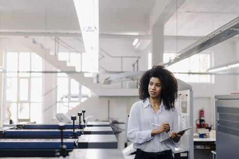 Afro female entrepreneur looking away while working with digital tablet in industry - KNSF08781