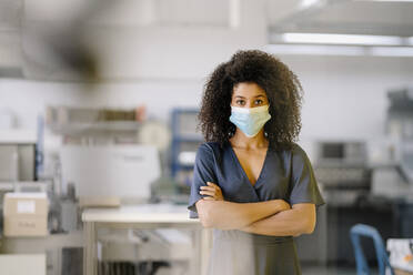 Mid adult businesswoman wearing protective face mask standing in industry during COVID-19 - KNSF08788