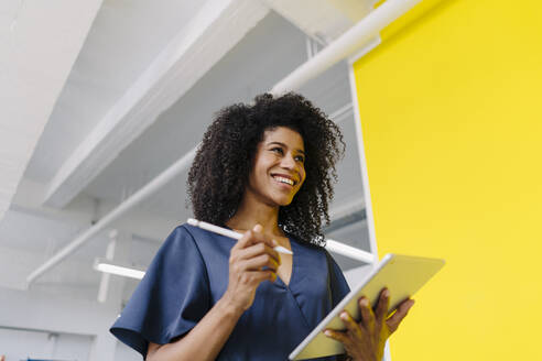 Smiling businesswoman holding digital tablet and digitized pen in industry - KNSF08794