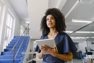 Businesswoman looking away while holding digital tablet in industry - KNSF08795