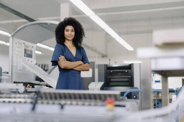 Female professional with arms crossed standing by machinery in industry - KNSF08813