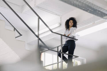 Female professional with arms crossed contemplating while leaning on railing at industry - KNSF08822