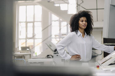 Unternehmerin mit Hand auf der Hüfte bei der Arbeit mit Druckmaschinen in der Industrie - KNSF08842