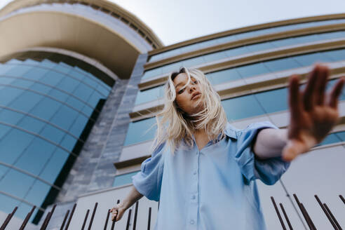 Young blond woman gesturing while standing in front of building - TCEF01935