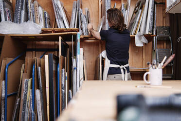 Männlicher Ladenbesitzer nimmt bei der Arbeit in der Werkstatt einen Bilderrahmen aus dem Regal - ASGF00497
