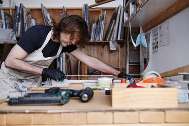 Reifer männlicher Ladenbesitzer bei der Herstellung von Bilderrahmen, während er am Tisch in der Werkstatt arbeitet - ASGF00508