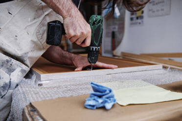 Handwerker mit Nagelpistole bei der Herstellung eines Holzrahmens in der Werkstatt - ASGF00509