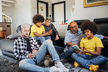 Multiethnische Familie benutzt Smartphones, während sie zu Hause im Wohnzimmer zusammensitzen - MEUF03122