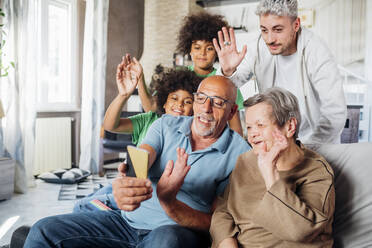Multiethnic family waving hands together while doing video call through smart phone at home - MEUF03134