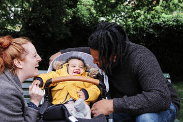 Glückliche Eltern spielen mit ihrem Sohn im Kinderwagen im Park - ASGF00519