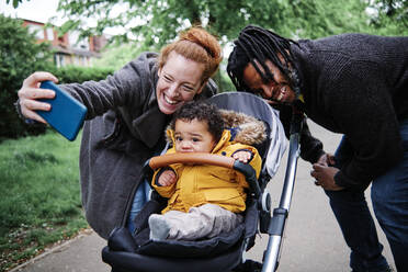 Fröhliche Eltern machen ein Selfie mit ihrem Sohn im Kinderwagen im Park - ASGF00523