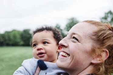 Smiling mother looking away while carrying son at park - ASGF00528