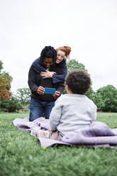 Mother embracing man photographing son sitting at parks - ASGF00561