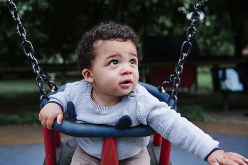 Kleiner Junge schaut weg, während er auf einer Schaukel auf dem Spielplatz sitzt - ASGF00566