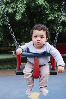 Niedlicher kleiner Junge schwingt auf einer Schaukel auf einem Spielplatz im Park - ASGF00567