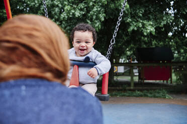 Lächelnder Junge beim Schaukeln auf dem Spielplatz im Park - ASGF00568