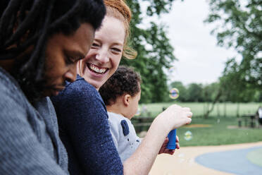 Smiling mother with son looking at man while playing with bubbles at park - ASGF00577