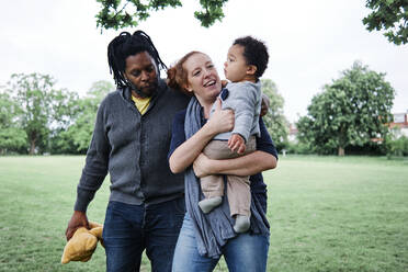 Mother looking at son while walking with man at park - ASGF00584