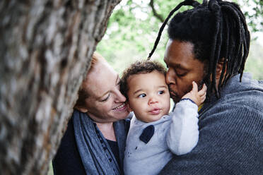 Glückliche Familie küsst süßen Sohn im Park - ASGF00588