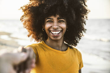 Afro-Frau lächelt, während sie die Hand ihres Freundes am Strand hält - DAF00051