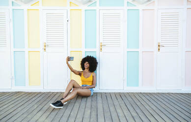 Smiling woman taking selfie in front of beach hut - DAF00053
