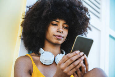 Junge Afro-Frau, die eine Textnachricht über ihr Mobiltelefon verschickt - DAF00054