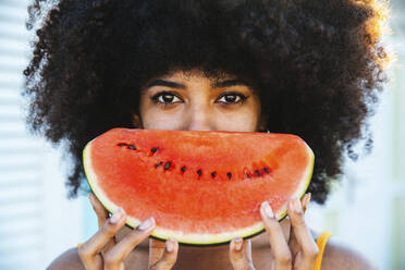 Afro-Frau, die ihr Gesicht mit einer Scheibe Wassermelone bedeckt - DAF00060