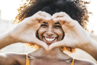 Smiling woman with heart shape from hands at beach - DAF00068