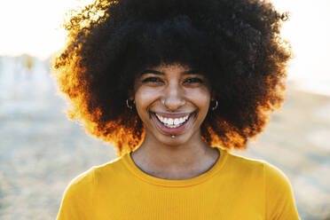 Smiling woman with Afro hairstyle at beach during sunset - DAF00071