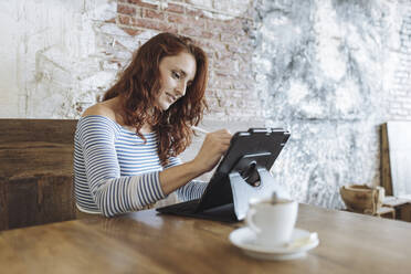 Weibliche Grafikdesignerin benutzt ein Tablet, während sie im Café sitzt - MTBF01024