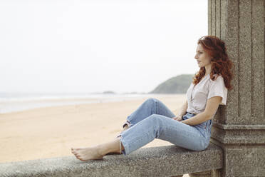 Redhead woman sitting on retaining wall during day - MTBF01045